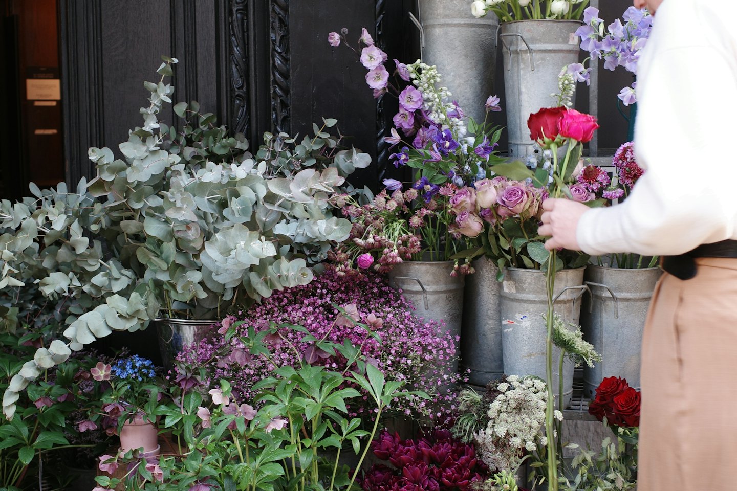 Florist arranging colorful flowers in buckets outside a shop.
